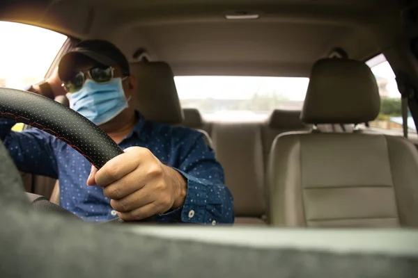 Blur male wearing a face mask, black glasses, and a black hat. Closeup hands of a man holding the steering wheel to control the car, are Upset while traffic congestion daylight. Blurred background