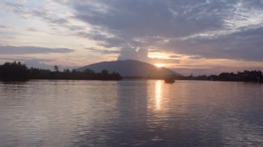 Gün doğumu ve nehir çekim yapıyor. Sabah dağdan gün doğumları ve nehirde tekneler var. Güneşten gelen altın ışık suya yansıdı. Çok güzel bir parıltı. Bulutlu gökyüzü.