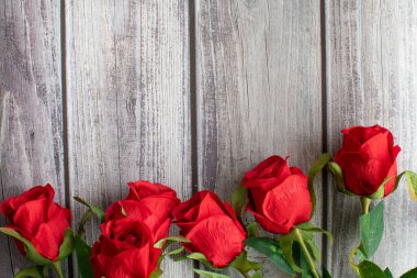 Sevgililer Günü konseptinin en üst noktası. Kırmızı gül çiçeği ve köşedeki ahşap masada güzel yeşil yapraklar. Yakın plan, Seçici odak, tasarım için sağdaki boşluğu kopyala, metin. Ahşap arkaplan