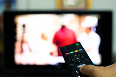 Adam elinde tutuyor ve TV 'yi açmak ve gece izlemek için kumandaya basıyor. Geceleri oturma odasında TV 'de film izlerim. Geceleri bir bakımevinde televizyonu aç. Seçici odaklanma. Yakın çekim.