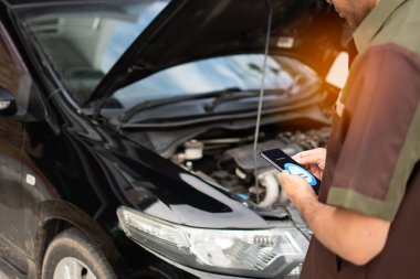 Yağ işlev monitörünü izlemek için akıllı telefonu tutan teknisyen. Mobil cihaz ekranında yakıt yağı durumu görünüyor. Araba tamiri için dijital teknoloji cihazları kullanma kavramı. Seçici odaklanma. Bulanık arkaplan