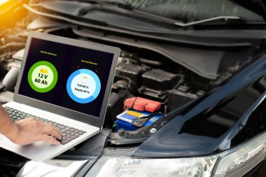 Kapanış, garajdaki araba motorunun çalışmasını kontrol etmek için dizüstü bilgisayarın klavyesinde yazan bir adam. Bir arabanın motoru çalışmaz. Bilgisayar ekranında pil ve yağ durumu görülüyor