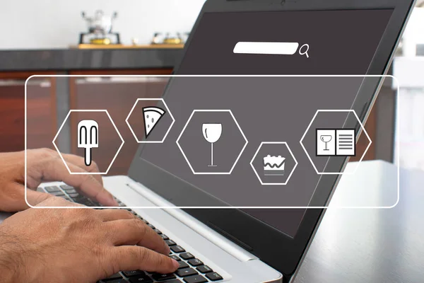 Closeup, A man\'s hand is typing on a laptop keyboard to search out how to cook. notebook computer white screen on the table. Has a pot on the gas stove. Blurred background, moke up, clipping path