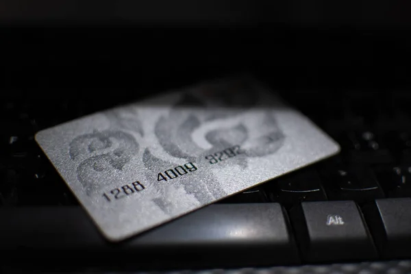 A credit or debit card grey placed on the computer keyboard black. The concept of online shopping with the Internet. Closeup. Selective focus. Blurred background.