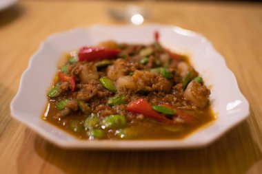 Tahta masadaki beyaz tabakta karides ezmeli baharatlı köri ve karides ezmesi. Taylandlılar arasında deniz ürünleri çok popülerdir. Yakından ve eğim açısından bak. Seçici odaklanma. Bulanık arkaplan.