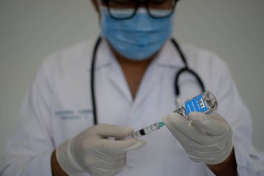 Doktorlar koronavirüse karşı aşı deneyleri yapıyorlar. Bilim adamları şırınga kullanıyorlar. Maske takan bir adam şırınga ve aşı şişesi tutuyor. Laboratuvar aşısı denemesi kavramı.