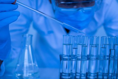 Biyokimyagerler yeni ilaçlar keşfetmek için deneyler yapıyorlar. Araştırmacılar bilim laboratuarlarında çalışırlar. Koruyucu gözlük ve bahçe eldivenleri takan erkek bir bilim adamı aşıyı test etmek için kimyasallar damlatıyor..