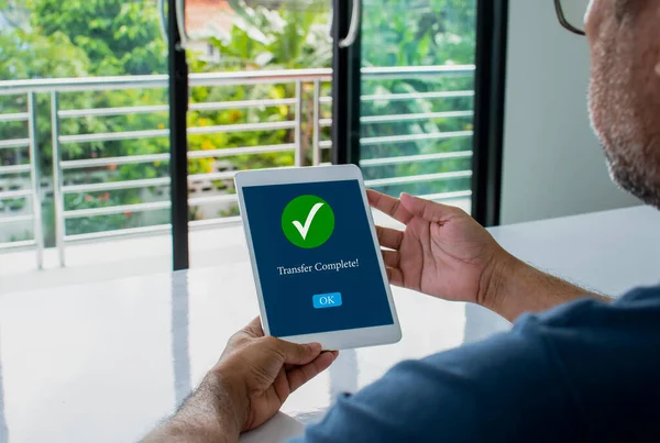 Tablet ekranda, ödemenin çevrimiçi alışveriş için başarılı olduğunu doğrulamak için tam bir aktarım mesajı gösteriliyor. Bir adam oturur ve elinde bir tablet tutar. Mobil cihazla alışveriş kavramı. Bulanık arkaplan