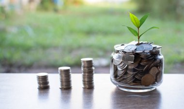 Bozuk parayı cam kavanoza koyup madeni paranın üzerine yerleştiriyorum. Bahçedeki ahşap bir masaya yerleştirilmiş bozuk para kavanozu. Bir blokta bir sürü bozuk para düzenlenir. - Yakın çekim. Tasarım için alanı kopyala. Bulanık arkaplan