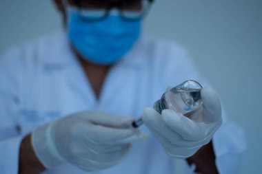 Maske takan bir adam şırınga ve aşı şişesi tutuyor. Laboratuvar aşısı denemesi kavramı. Doktorlar koronavirüse karşı aşı deneyleri yapıyorlar. Bilim adamları şırınga kullanıyorlar..