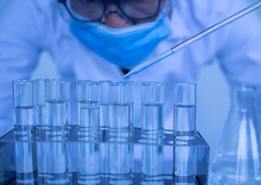 Koruyucu gözlük takan ve eldiven takan bir erkek bilim adamı aşıyı test etmek için kimyasallar damlatıyor. Biyokimyagerler yeni ilaçlar keşfetmek için deneyler yapıyorlar. Araştırmacılar bilim laboratuvarlarında çalışırlar..