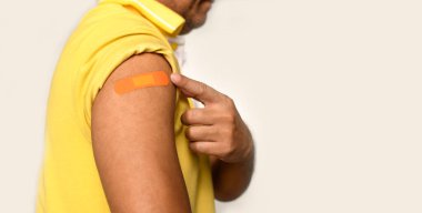 Adamın koluna turuncu bir alçı yapıştırılmış. Coronavirus (COVID-19) aşısı sonrası ilk yardım kavramı ve profesyonel, tıbbi, iğne, kan, kanser. Yakın plan, beyaz bulanık arkaplan