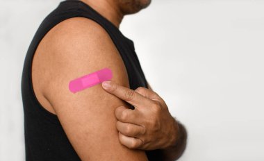 Adamın koluna turuncu bir alçı yapıştırılmış. Coronavirus (COVID-19) aşısı sonrası ilk yardım kavramı ve profesyonel, tıbbi, iğne, kan, kanser. Yakın plan, beyaz bulanık arkaplan