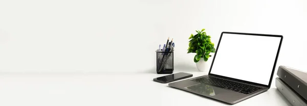 Blank white screen laptop on a white table in the office. Working concept using technology smartphones, notebook, internet. Copy space on left for design or text, Closeup, Gray, and blurred background