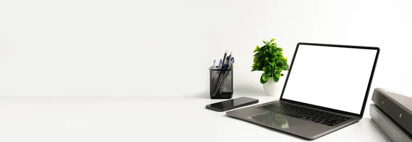Ofisteki beyaz masadaki boş beyaz ekran dizüstü bilgisayar. Teknoloji akıllı telefonları, defter ve internet kullanarak çalışıyor. Tasarım veya metin için sol tarafta boşluk kopyala, Kapat, Gri ve bulanık arkaplan