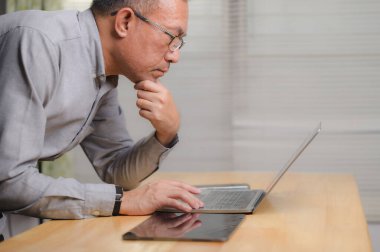 Ciddi bir orta yaşlı iş adamı. Gözlük takıyor. Elleri çenesinde masaya yaslanıyor. Bilgisayardaki verileri analiz ediyor..