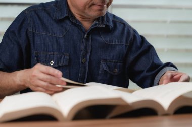 Kot gömlek giyen odaklanmış orta yaşlı bir adam masada büyük açık bir kitap okur, hayat boyu öğrenmeyi, sürekli eğitimi, sessiz kütüphane ortamında kendini geliştirmeyi temsil eder..