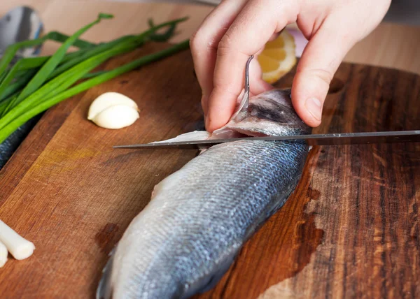 Processo de cozinhar peixe. Mãos cozinhar cortar o peixe em uma tábua de corte de madeira — Fotografia de Stock