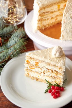 Noel pastası dilimi hindistan cevizi ve şeftali ile süslenmiş yaban mersini ve biberiye beyaz tabakta.