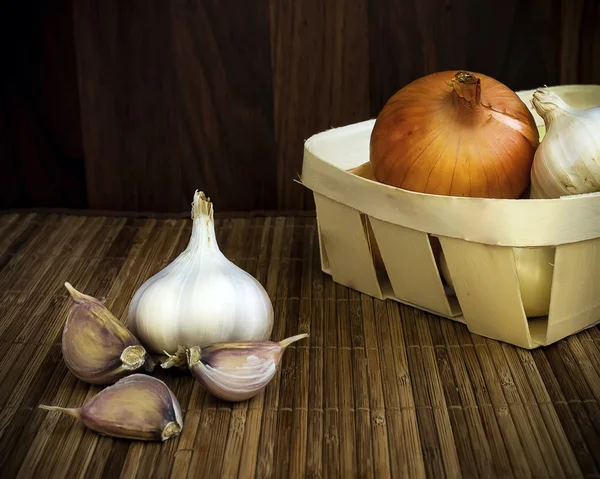 Raw garlic and onion in a rustic woven straw basket, on a wooden background — Stock Photo, Image
