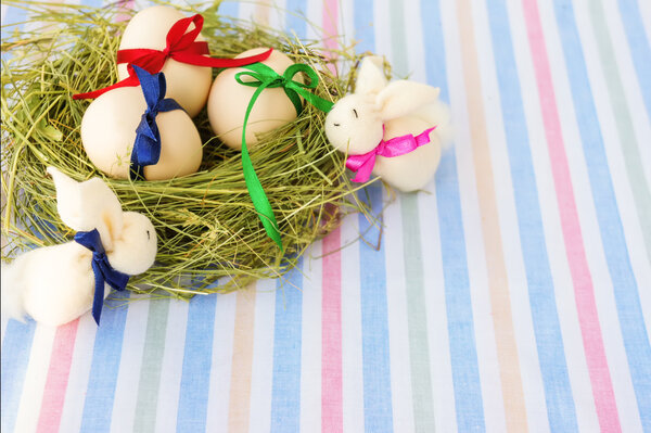 Easter eggs and rabbit in nest on stripe textile background
