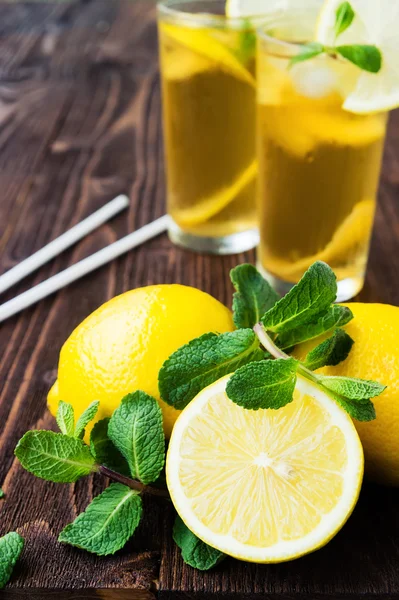 Limones con menta y dos vasos de té helado sobre mesa de madera —  Fotos de Stock