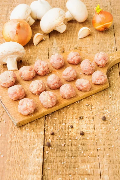 Albóndigas crudas en un tablero de madera con ingredientes —  Fotos de Stock