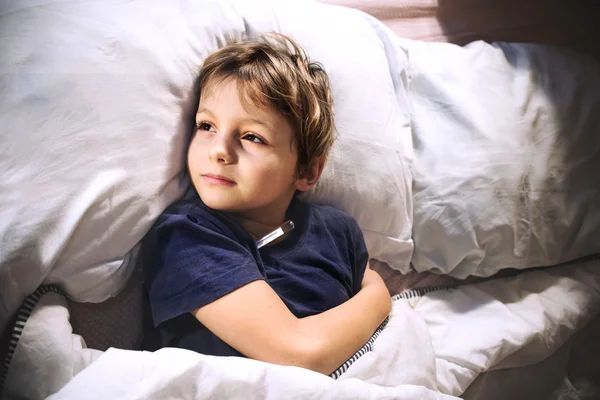 Niño enfermo en la cama con fiebre y termómetro —  Fotos de Stock
