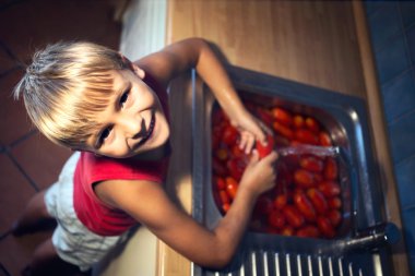 happy boy washes the tomatoes to prepare the organic sauce clipart