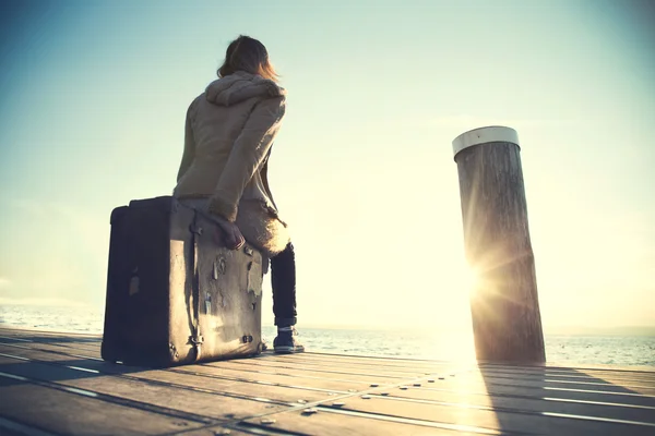 Vrouw zit op haar koffer wachten op de zonsondergang — Stockfoto