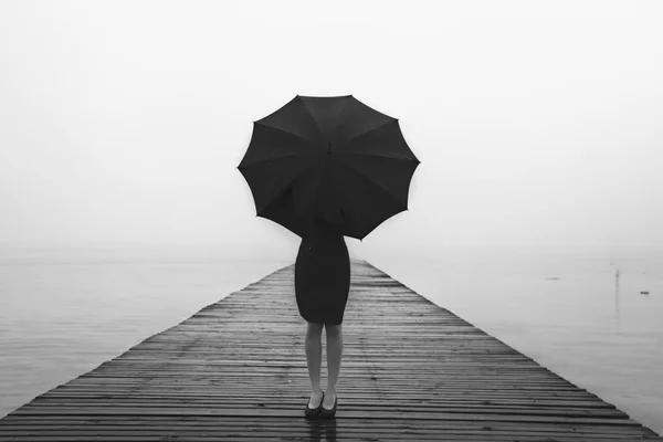 Frau in Schwarz versteckt sich mit Regenschirm in einer nebligen Landschaft — Stockfoto