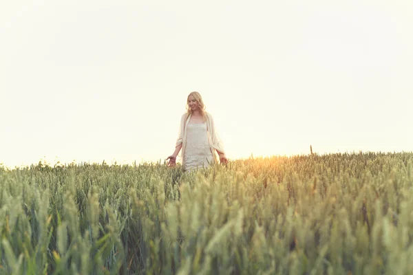 Jovem mulher andando em um campo de trigo no pôr do sol — Fotografia de Stock