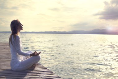Gün batımında kumsalda yoga yapan kadın.