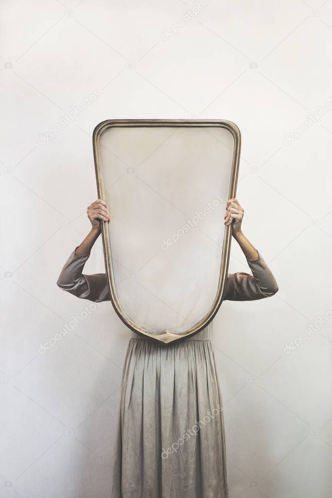 woman hides holding a mirror in front of her face; introspection concept