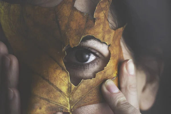 woman hides her face with an autumn leaf, artistic and creative portrait