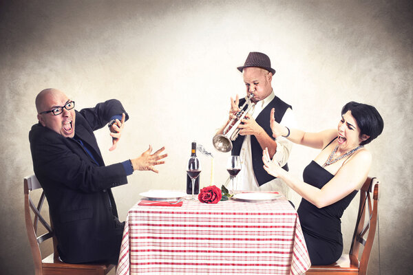 Angry couple disturbed by a trumpet musician while having dinner