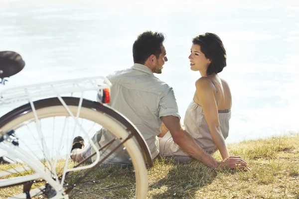 Casal com bicicleta descansando em frente ao lago — Fotografia de Stock