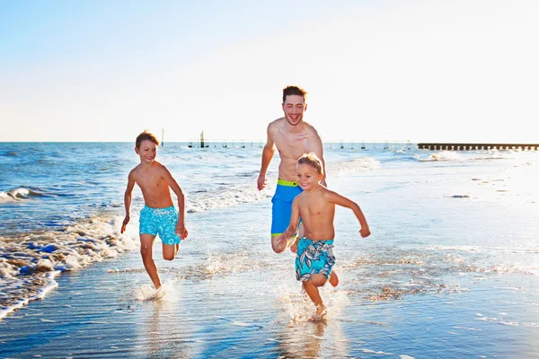 Far och söner som spelar på stranden — Stockfoto