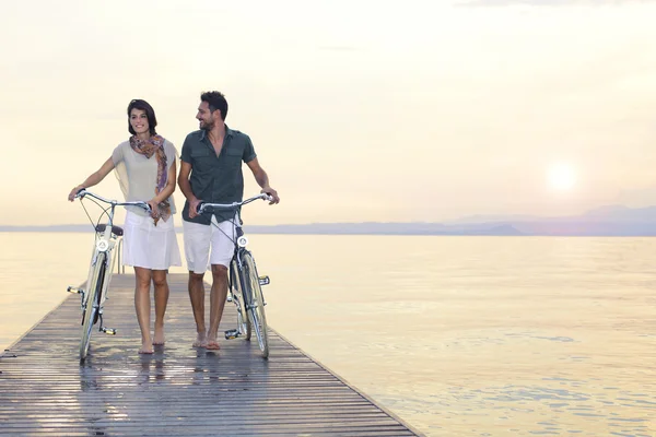 Coppia innamorata spingendo bici su una passerella al lago — Foto Stock