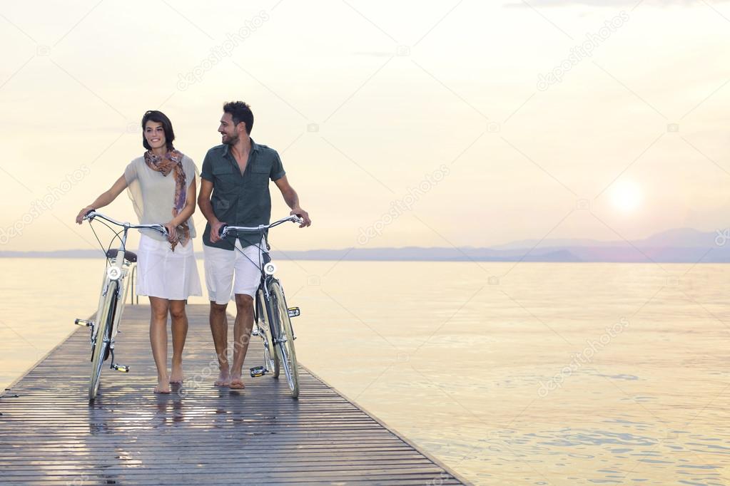 Couple in love pushing bike on a boardwalk at the lake