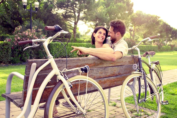 Casal apaixonado sentado togheter em um banco com bicicletas ao lado — Fotografia de Stock