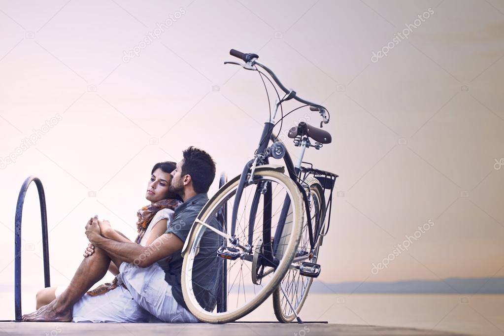 Couple in love resting on a boardwalk with a bike at the lake