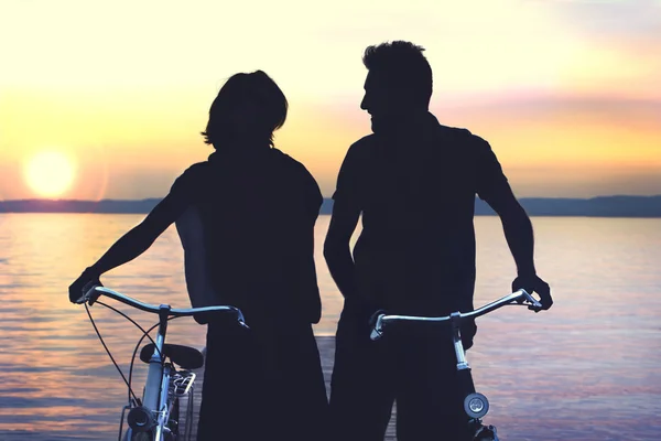 Silouette von Paar, das Fahrrad auf einer Promenade bei Sonnenuntergang trägt — Stockfoto