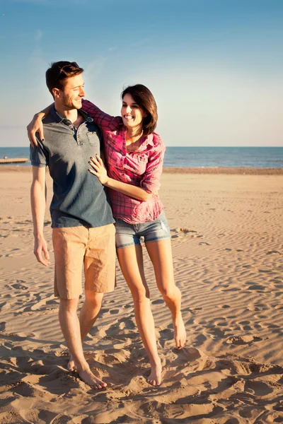 Lachende paar wandelen langs het strand bij zonsondergang — Stockfoto