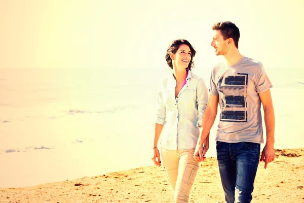 Casal feliz andando ao longo da praia ao pôr do sol — Fotografia de Stock