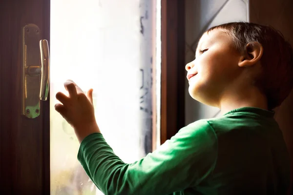 Concentrated child writes with his fingers on the foggy window — Stock Photo, Image