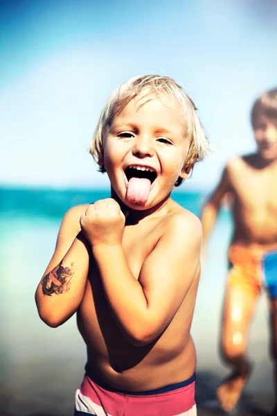 Grappige jongen maakt de tong op het strand — Stockfoto