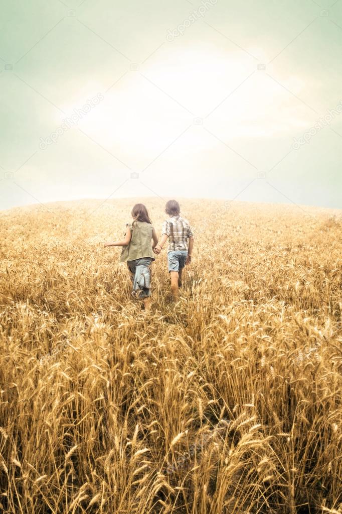 Children running into wheat to the sunset