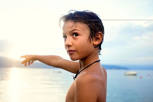 Young boy standing pointing into the sky in front of sea — Stock Photo, Image