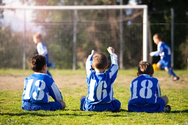 Niños jóvenes en uniforme viendo a su equipo mientras juegan al fútbol — Foto de Stock